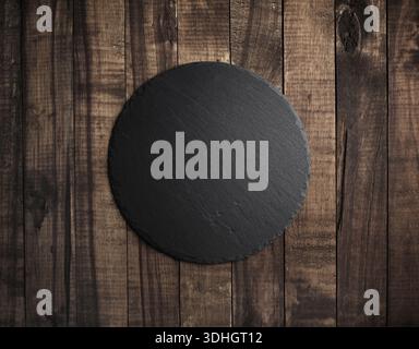 Blank black round stone slate plate on wooden textured surface. Copy space. Flat lay. Stock Photo