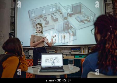 Caucasian Young Adult Woman Presenting Architectural Floor Plan to Diverse Team Stock Photo