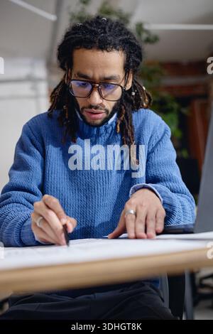Young Adult Black Man Writing on Paper While Working at Desk Indoors Stock Photo