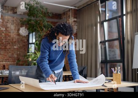 Young Adult Black Man Analyzing Construction Plans While Standing in Office Stock Photo