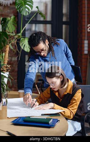 Young Caucasian Woman Collaborating with Young Black Man on Architectural Plans Stock Photo