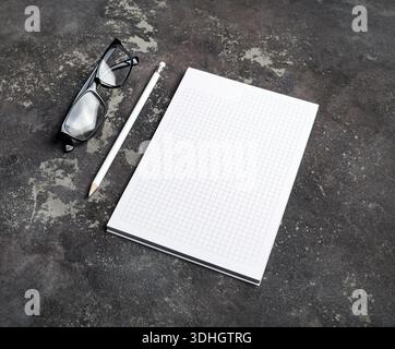 Blank notebook, glasses and pencil on concrete surface. Branding stationery mockup. Stock Photo