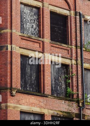 Old red brick building with boarded-up windows showing signs of decay and neglect in a European city. Symbolic image of urban decline, abandonment and Stock Photo