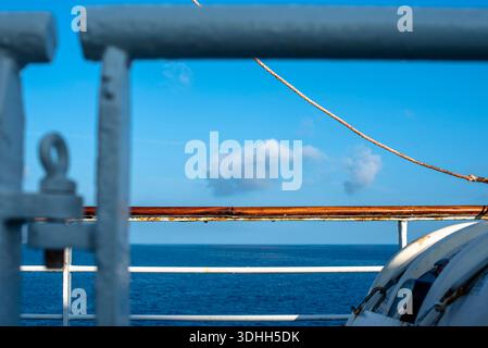 Metal railings and a rope line on a ferry near Corsica, with the sea and clouds in the background. Clean nautical composition with subtle rust details Stock Photo