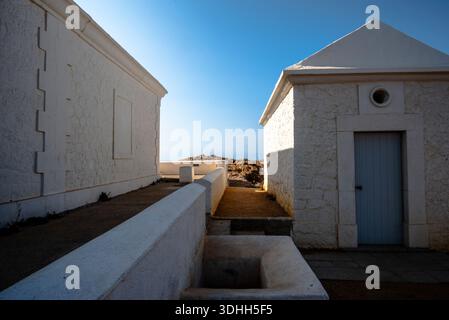 Narrow passage between white stone buildings leading toward rocky coastline and the Mediterranean Sea in Corsica, with dramatic light and shadows. Stock Photo