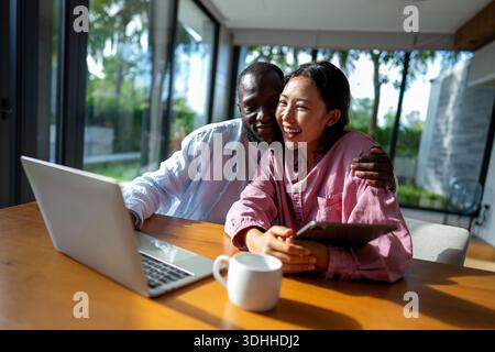 Young happy multiethnic couple having fun while using laptop at home. Happy couple discussing future Stock Photo