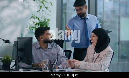 Three business colleagues. Businessman with Islamic businesswoman discuss talking working looking computer Arabian man leader boss come in office Stock Photo