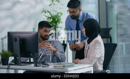 Three Muslim colleagues Arabian office workers Indian managers business team talking discuss job task teamwork at workplace strategy planning work Stock Photo