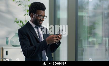 African American businessman smiling looking at smartphone in modern office happy male professional business man reading message using mobile phone Stock Photo