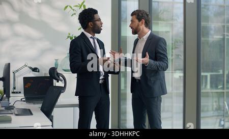 Two multiracial businessmen emotional discussing startup in office holding at digital tablet business men diverse male colleagues talking cooperation Stock Photo