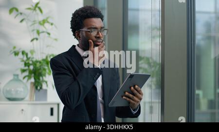 Thoughtful African American businessman in office concentrate using digital tablet looking out window focused business male man guy using technology Stock Photo