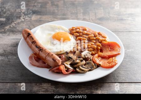 Full English breakfast with fried egg, bacon, sausages and beans on wooden table. Stock Photo