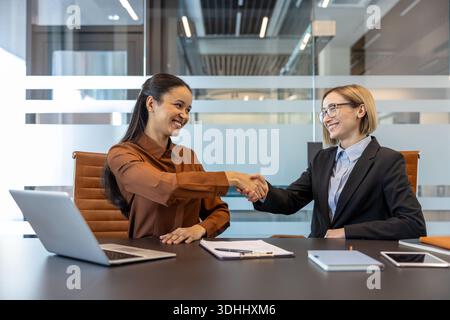 Two smiling multiethnic businesswomen performing a handshake, concluding a successful partnership agreement or a new recruitment during an office meeting Stock Photo