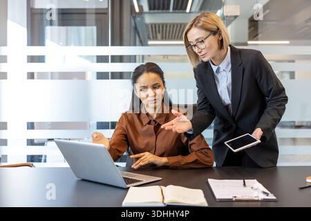 Two professional business women collaborating on a laptop project during a corporate meeting, discussing strategy and reviewing digital documents in a modern office workplace Stock Photo