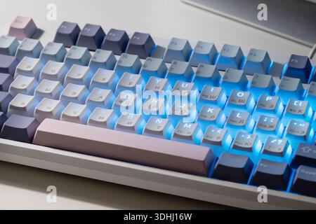 Mechanical keyboard with blue LED backlight on desk, modern technology workspace concept. Stock Photo