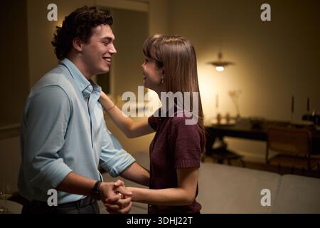 Young Caucasian man and young Caucasian woman smiling while holding hands and dancing together in living room, both appearing happy and engaged in conversation Stock Photo
