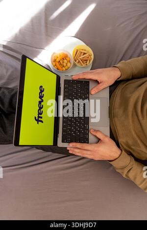 Bar, Montenegro, 22 January 2026, Man watching movie on Freevee platform site on laptop while sitting on bed at home Stock Photo