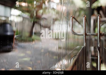 A shallow depth of field shot focusing on water droplets running down a clear glass surface, with a bokeh effect showing a blurred outdoor garden Stock Photo