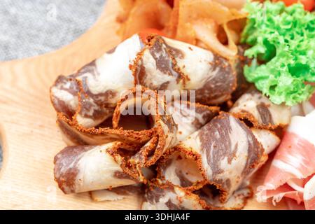 An extreme close-up shot of rolled-up, thinly sliced pieces of cured and dried spiced meat, such as basturma or sujuk. The focus is sharp on the rich Stock Photo