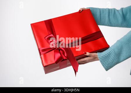 Closeup hands presenting red wrapped gift with ribbon on white background, ideal for ecommerce banner, website hero, or social promo. Stock Photo