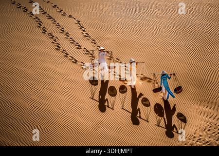 Aerial view of three figures traversing the undulating dunes, their shadows stretching long across the rippled sand, creating a stark contrast between Stock Photo