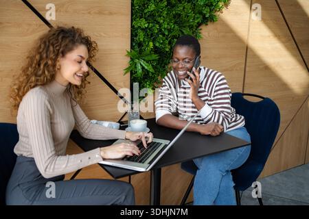Women collaborating using laptop and smartphone in a modern cafe Stock Photo