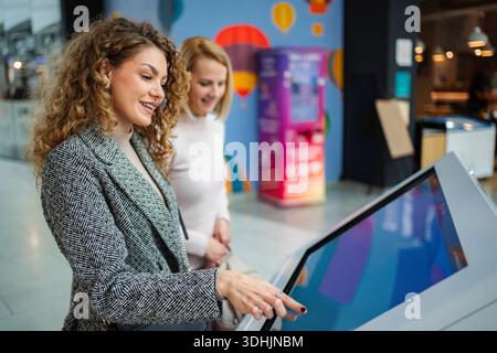 Women friends using interactive digital kiosk touch screen Stock Photo