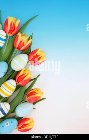 Easter egg, red yellow tulip flower seasonal background decoration on gradient blue white. Sweet candy treats with painted eggs for fun holiday season Stock Photo