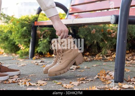Close-up of a person's hand carefully holding stylish tan leather combat boots with a durable chunky lug sole, perfect for versatile autumn fashion an Stock Photo
