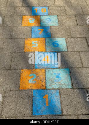 A colorful hopscotch grid numbered 1 to 10 painted on gray stone pavement in the sunlight. Stock Photo