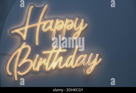A neon sign that says Happy Birthday. The sign is lit up and has a yellow glow. The sign is on a blue background Stock Photo