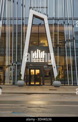 VINKOVCI, CROATIA, 12.13.2025:A contemporary library exterior featuring a striking white arch entrance set within glass panels. Warm interior lighting Stock Photo