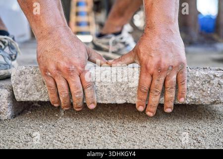 Installing new pavement or floor outside from large concrete tiles, closeup detail on male worker fitting stone block over sand and gravel base layer Stock Photo