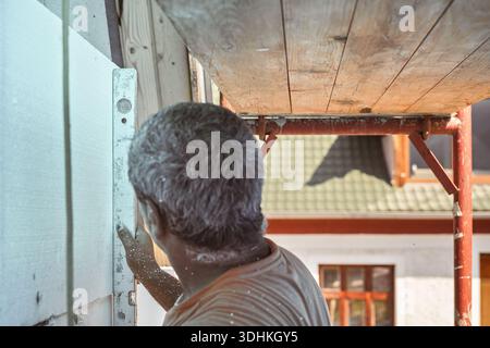 Construction worker using spirit level to measure foam insulation installed on a house wall, view from behind Stock Photo