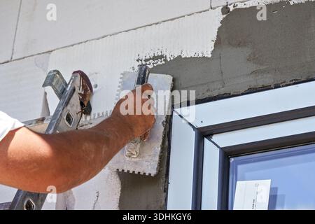 Construction worker applying top layer of plaster next to newly installed window closeup detail during house construction Stock Photo