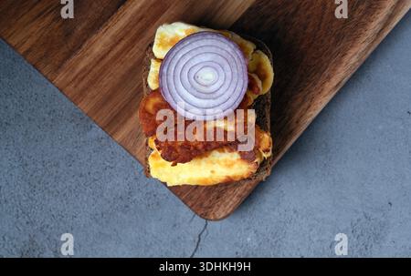 A minimalist top-down view of a single slice of toasted bread with grilled halloumi cheese and a fresh red onion slice on a wooden surface Stock Photo