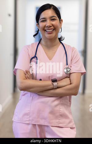Female nurse standing in clinic hall wearing pink scrubs, stethoscope, smartwatch, smiling Stock Photo