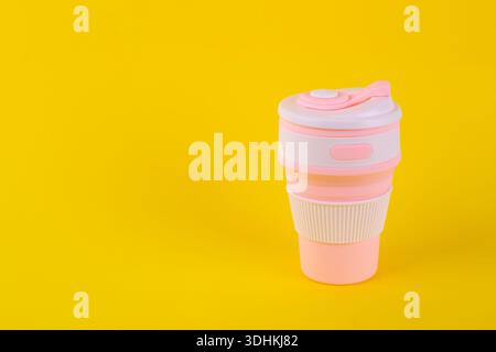 reusable pink silicone cup. folding cup isolated on yellow background. replacement of plastic cup Stock Photo