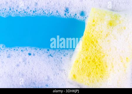 Cleaning yellow sponge and a soapy bubble foam on a blue background. Cleaning concept, cleaning service. Banner. Flat lay, top view Stock Photo