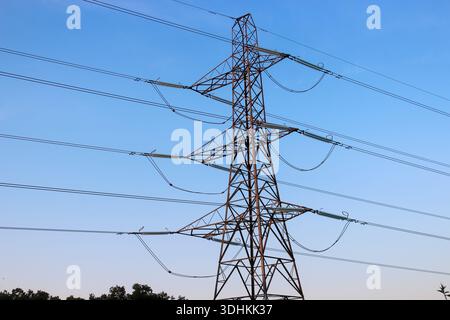 Large steel lattice transmission tower (pylon) set against a clear blue sky, supporting multiple high-voltage power lines via long glass insulators. Stock Photo