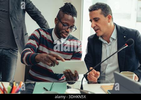 Two colleagues discussing data on a tablet during a business meeting. Concept of collaboration, teamwork, strategy and professional decision making in Stock Photo