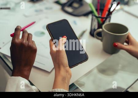 Colleagues discussing work tasks using a smartphone during a business meeting. Concept of collaboration, communication, planning and modern office wor Stock Photo