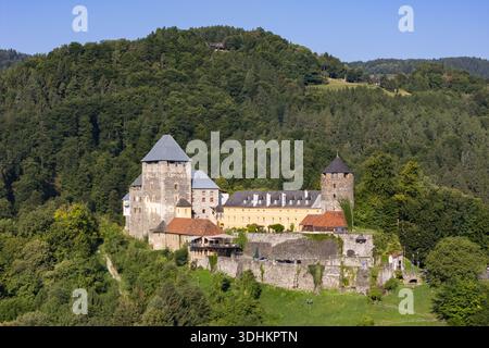 Aerial view of the formidable Burg Deutschlandsberg castle, a medieval fortress with grey stone walls and red tiled roofs amidst lush green forests, D Stock Photo