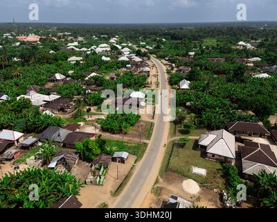 Aerial view of a long straight road cutting through the lush green canopy of trees and rooftops, Eberi, Rivers, Nigeria. Stock Photo