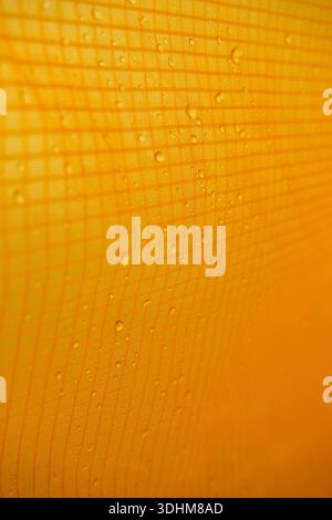 Rain droplets on waterproof tent fabric, creating a detailed outdoor textile texture with grid pattern and warm tones, suitable for background Stock Photo