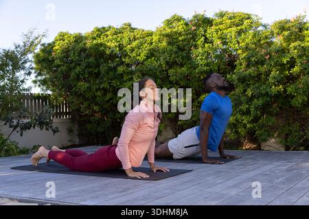 Couple practicing yoga doing upward back-bends on backyard deck on two dark mats, in athletic wear Stock Photo