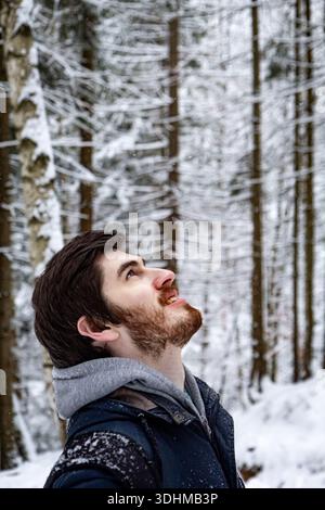 Vertical photo of a bearded dark haired man looking up in awe in a snowy forest. Calm winter portrait Stock Photo
