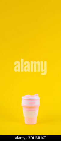 reusable pink silicone cup. folding cup isolated on yellow background. replacement of plastic cup Stock Photo