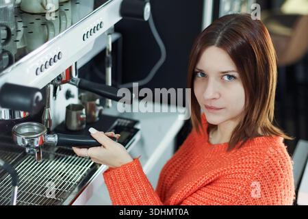 Focused barista in vibrant orange sweater crafting espresso drink using professional machine in cafe Stock Photo