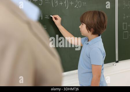 Schoolboy doing math on chalkboard in classroom Stock Photo